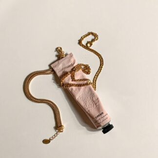 Tubo rosa de crema hidratante rodeado con una cadena de oro