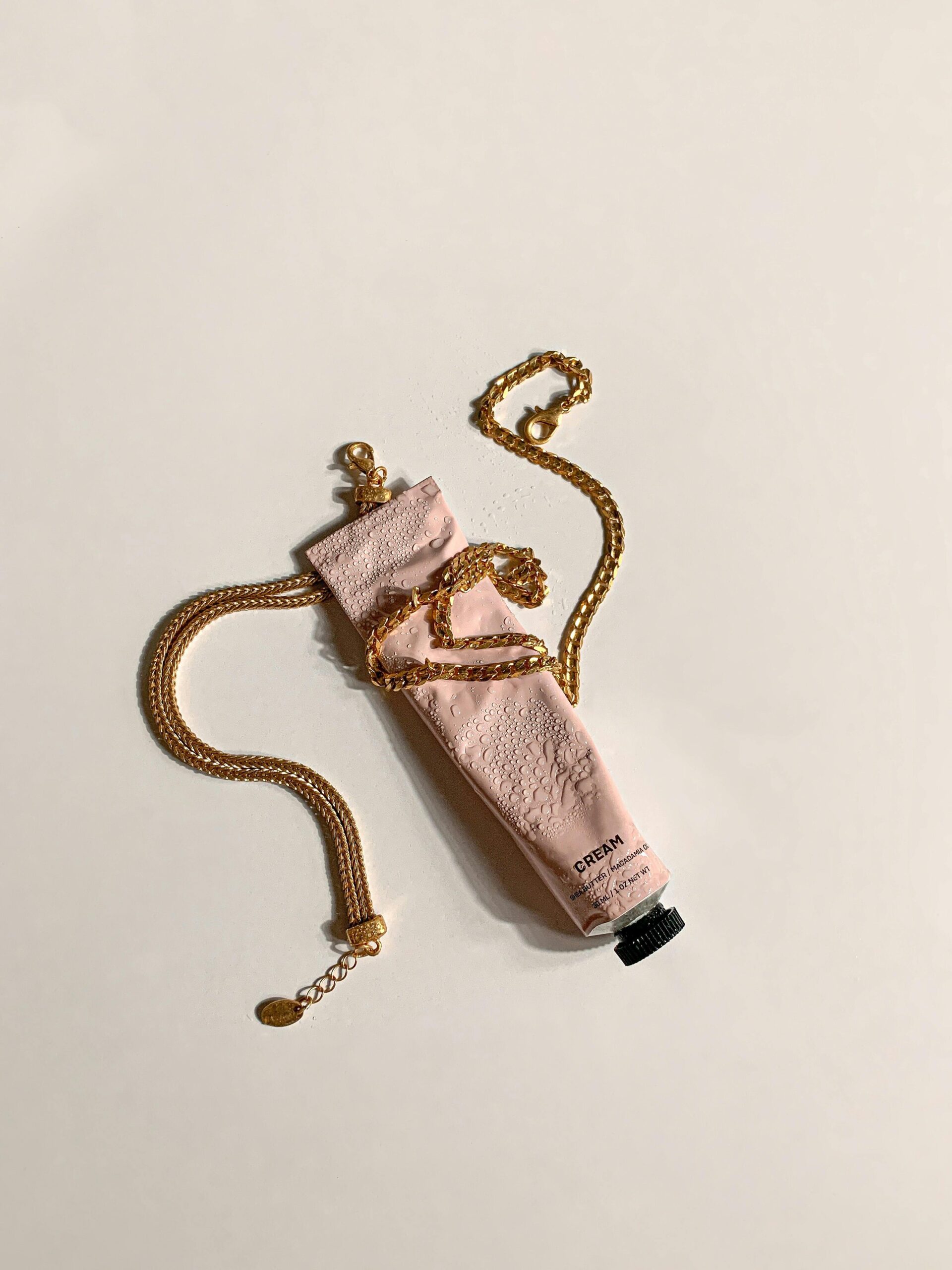 Tubo rosa de crema hidratante rodeado con una cadena de oro