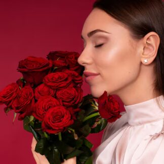 Chica posando con unas flores rojas y con los pendientes Rosas eternas en sus orejas.