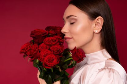 Chica posando con unas flores rojas y con los pendientes Rosas eternas en sus orejas.