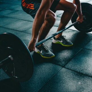 Barra olímpica levantada por un chico haciendo peso muerto en el gimnasio con el suelo de caucho.
