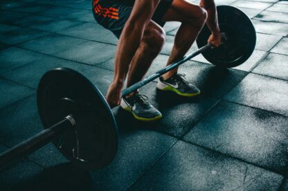 Barra olímpica levantada por un chico haciendo peso muerto en el gimnasio con el suelo de caucho.