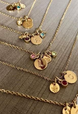 Joyas personalizadas con iniciales, cadenas doradas con chamrs de colores, encima de una mesa de madera