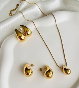 Para poder complementar tu look tenemos unos pendientes y un collar encima de una manta de seda color blanca y las joyas son de doradas