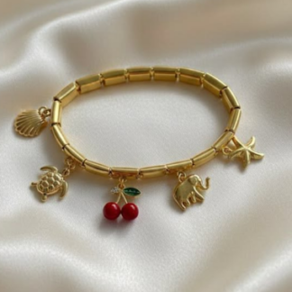 Pulsera dorada con charmes de temática veraniega con un fondo de un satín blanco