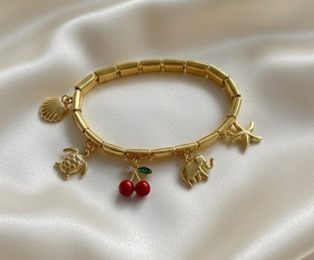 Pulsera dorada con charmes de temática veraniega con un fondo de un satín blanco